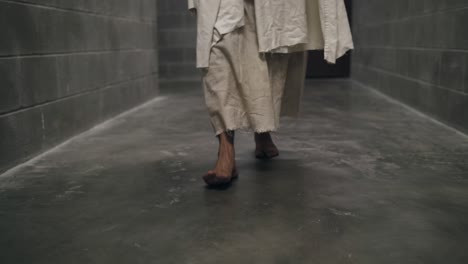 closeup of the feet of jesus wearing white robe walking in slow, dramatic fashion in prison hallway