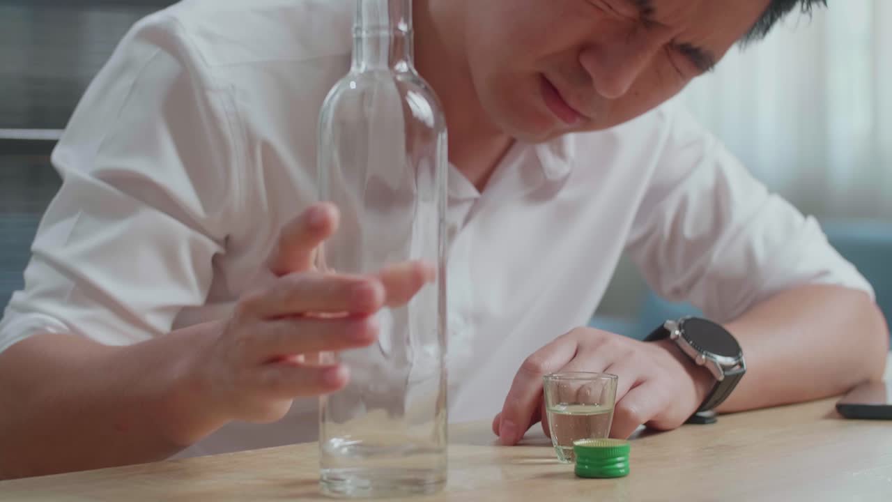 술에 취한 우울한 아시아 남자가 집에서 술을 마시기 전에 글라스에 보드카를 부어