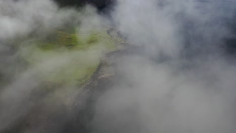 Rugged-Faroe-Islands-coastline-aerial-reveal-through-sea-clouds,-high-cinematic