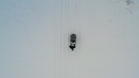 aerial top down view of female push baby carriage on snowy countryside road