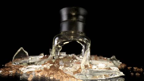 Pushing-towards-a-broken-sea-salt-grinder,-top-portion-standing-upright,-wide-angle-macro-view-of-the-broken-glass-and-salt-intermixed---salt-is-mesquite-flavored-hence-the-darker-color