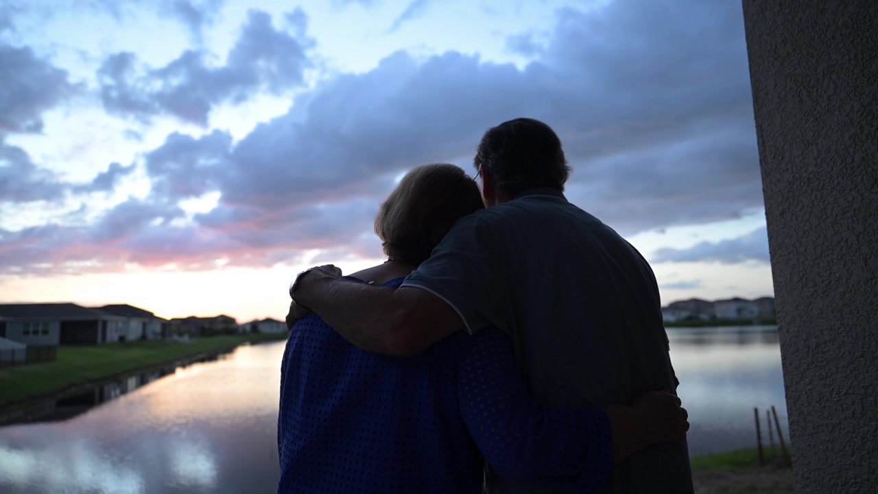 loving senior citizens embrace watching a beautiful sunset in their backyard after a strong storm
