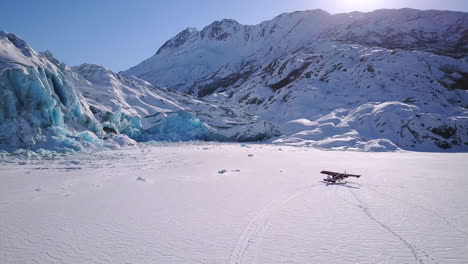 Aerial-flying-down-side-of-glacier-to-reveal-airplanes-parked-in-snow