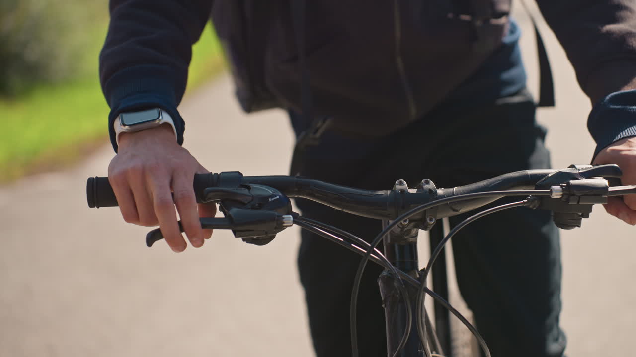 Rider controls bike carefully, Person manages bicycle with smartwatch precision, Cyclist on sunny trail skillfully controlling speed and direction with smartwatch and focused hands