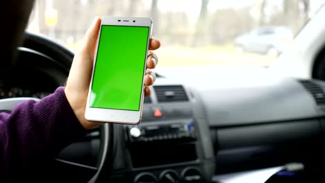 una mano sosteniendo un teléfono inteligente con pantalla verde en blanco en el coche para la dirección, masaje, ubicación, negocio. hombre se sienta en un coche moderno y trabaja en teléfono inteligente - pantalla verde - primer plano. llave de croma.