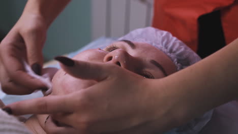 el cosmetólogo elimina las sobras de la máscara de alginato de la cara de la chica.