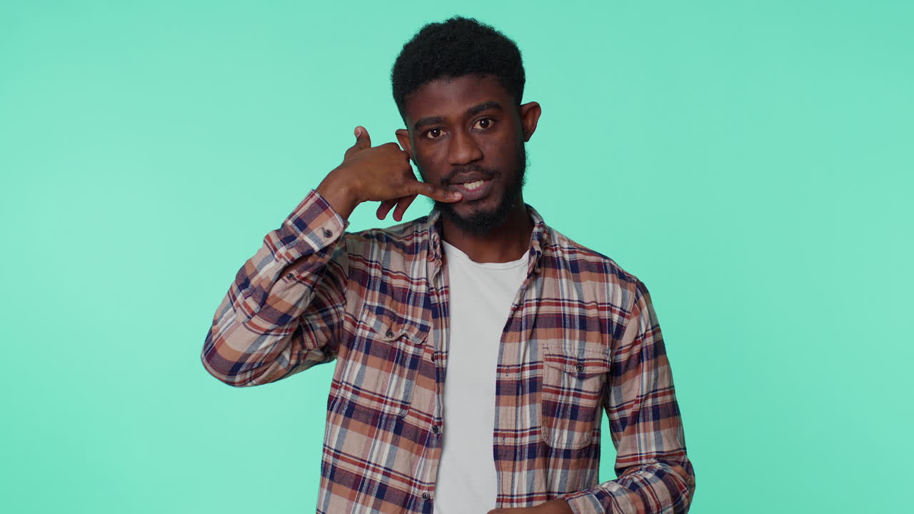 Cheerful african american man looking at camera doing phone gesture like says hey you call me back