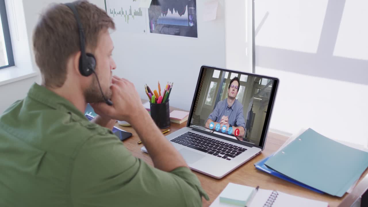 Kaukasisk mand bruger bærbar computer og telefonheadset på videoopkald med en mandlig kollega.