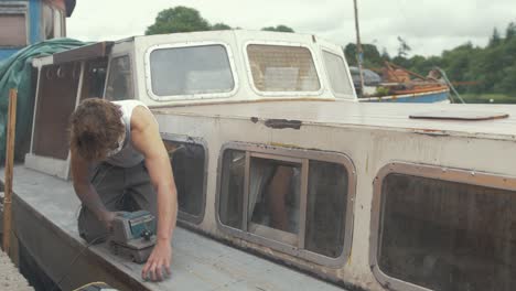 young working topless in summer sealing wooden boat cabin roof to prevent leaks