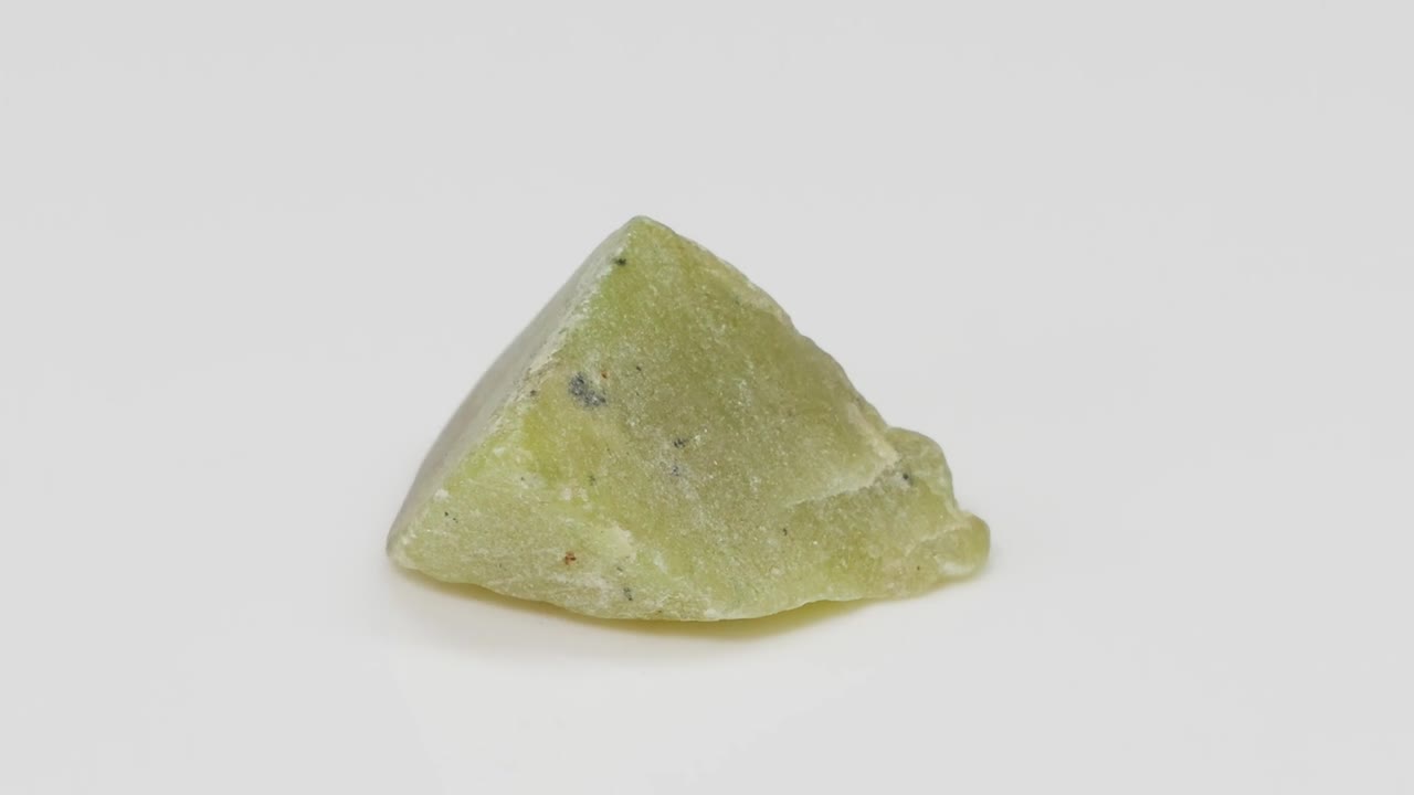 A green stone rotates, showcasing its texture and shape on a plain white background.