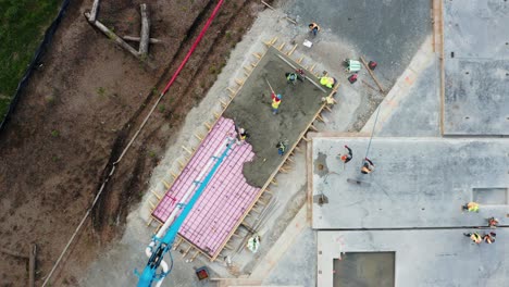 vista aérea de los trabajadores y el camión bomba de cemento de brazo largo que bombea la mezcla de cemento en la superficie del piso del edificio en construcción
