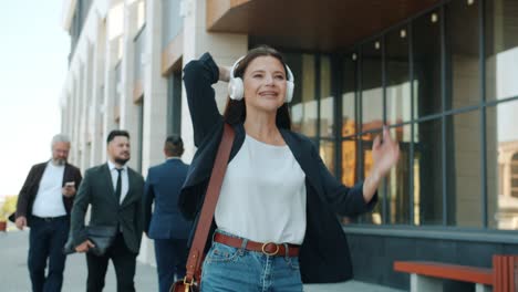 happy young business lady dancing walking outdoors wearing headphones outdoors in busy street