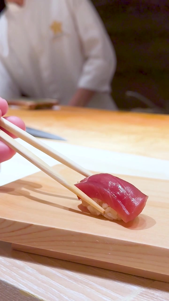 Un cliente usa bacchette di legno per prendere nigiri di tonno fresco da un tagliere di legno