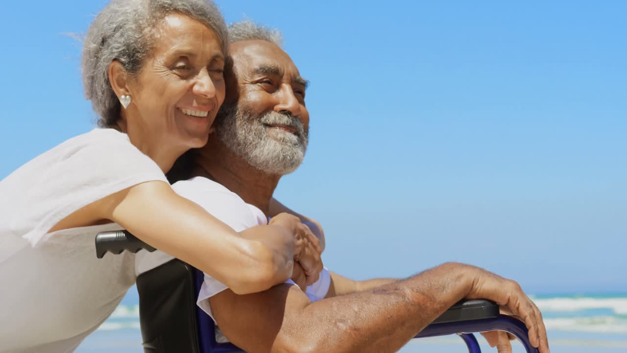Side view of active senior African American woman embracing disabled senior man on the beach 4k