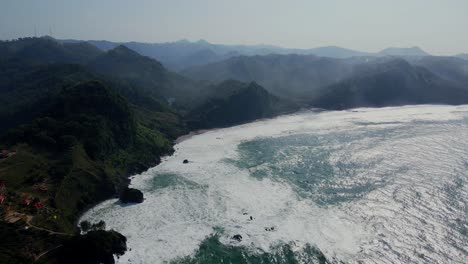 Toma-Cinematográfica-De-Drones-De-Olas-Gigantes-Del-Océano-Que-Alcanzan-Una-Hermosa-Costa-Con-Cordillera-En-Verano---Java-Central,-Indonesia---Estableciendo-Un-Vuelo-De-Drones