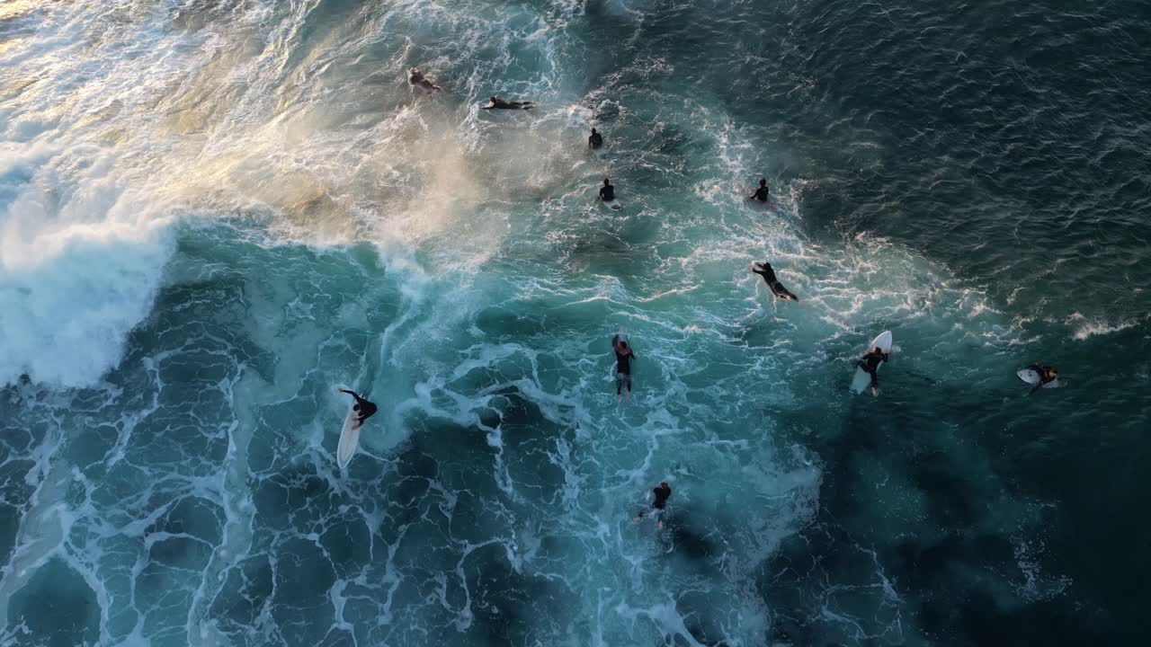 fotografía aérea de arriba hacia abajo de un surfista surfeando en una ola entre un grupo de surfistas en el océano índico durante la puesta de sol con los rayos del sol