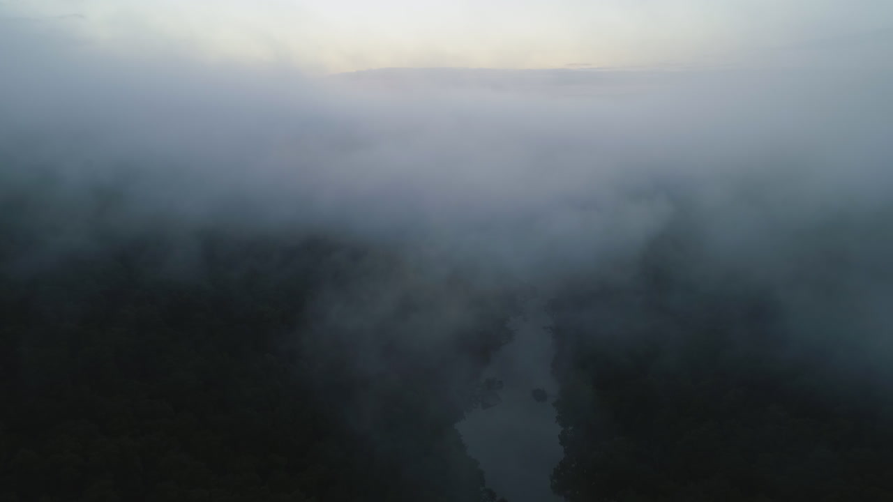 Aerial drone pushes from steep river valley into dense fog early morning, 4K