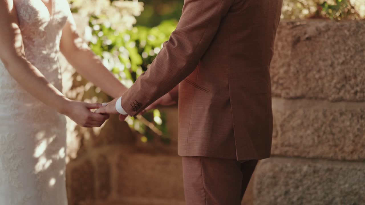 primer plano de una novia y un novio tomándose suavemente de las manos bajo una luz cálida