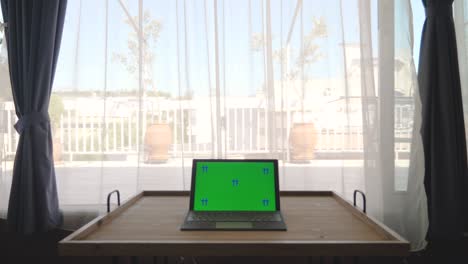 pantalla verde clave de croma de la computadora portátil colocada en la mesa de madera en el apartamento. cortinas de la ventana en el fondo. trabajando desde casa.