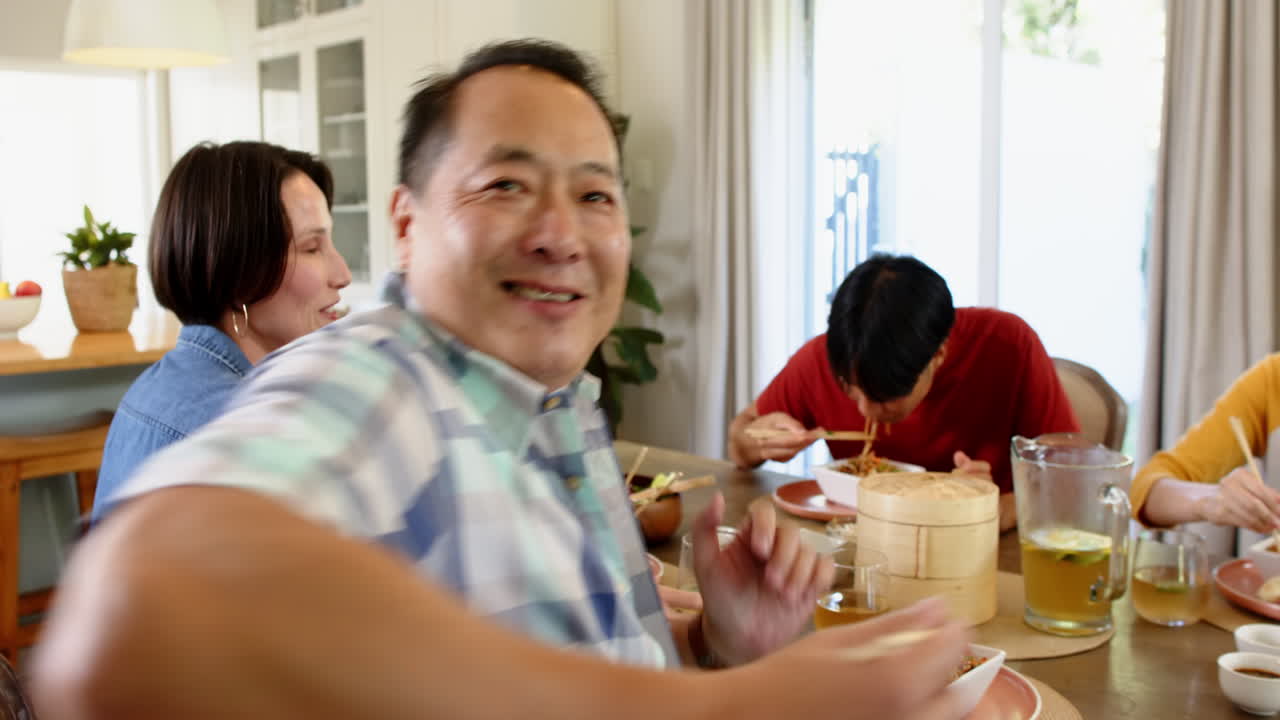 Eating noodles together, family enjoying meal at dining table with chopsticks