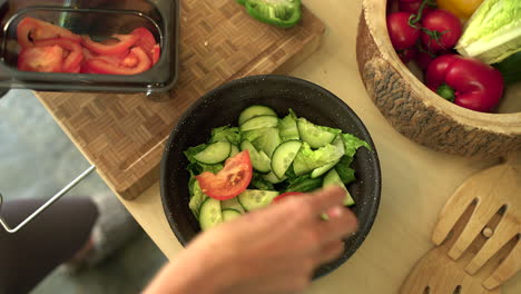 close up of female hands adding sliced tomato to salad bowl