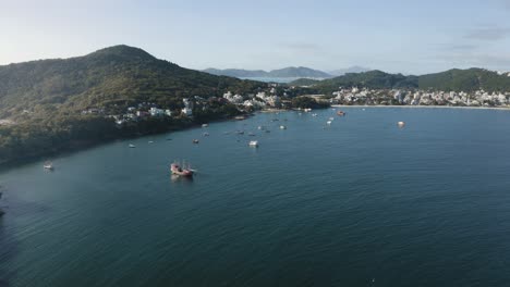 vista aérea avanzando sobre una montaña que revela una costa de playa paradisíaca con arena blanca y agua azul clara y profunda