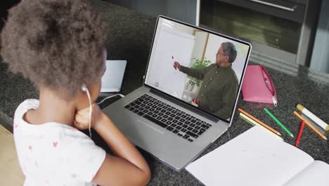 niña afroamericana usando portátil para llamada de video, con maestro masculino en la pantalla