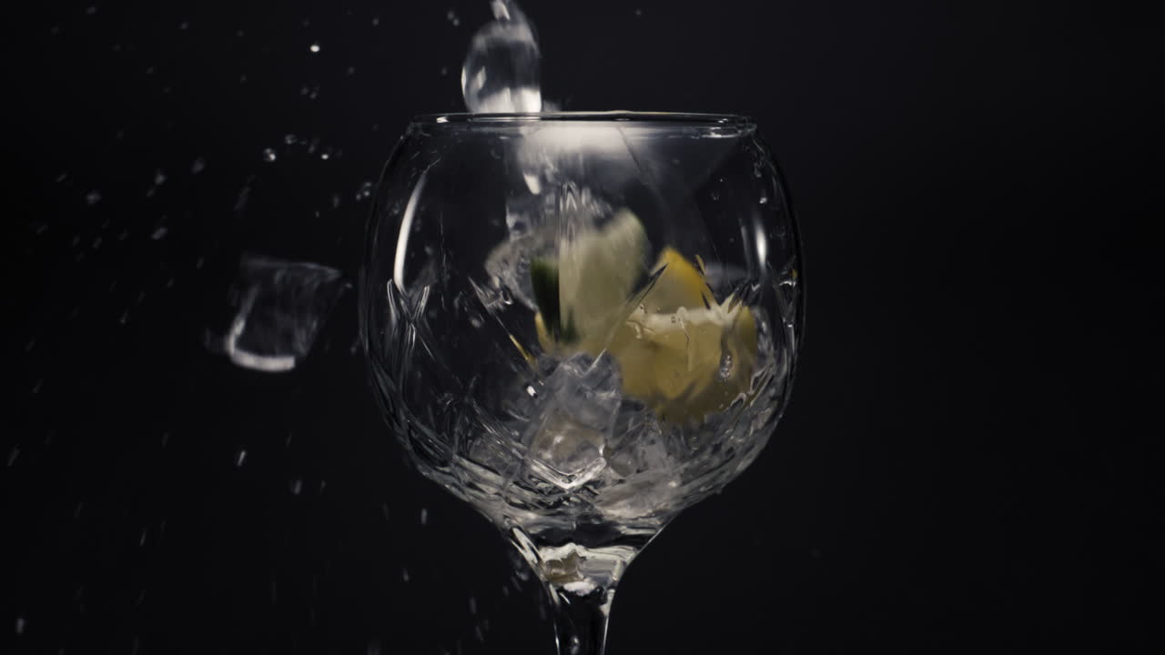 Cubetti di ghiaccio e limoni che cadono in un calice vuoto in primo piano. Concetto di bevanda rinfrescante.