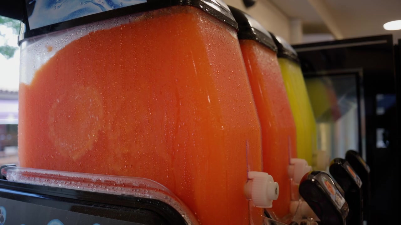 Dispenser fyldt med orange frossen slushice, der tilbyder en kold og forfriskende sommerdrik. Kondens på beholderen.