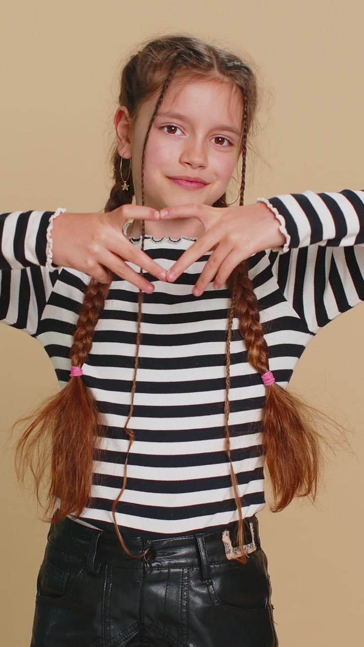 Una bambina sorridente fa un gesto con il cuore, dimostra il segno dell'amore, esprime buoni sentimenti e simpatia.