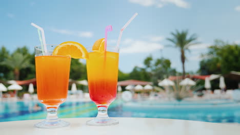 relax on the sun loungers near the pool with two exotic cocktails with straws blue sky and green pal