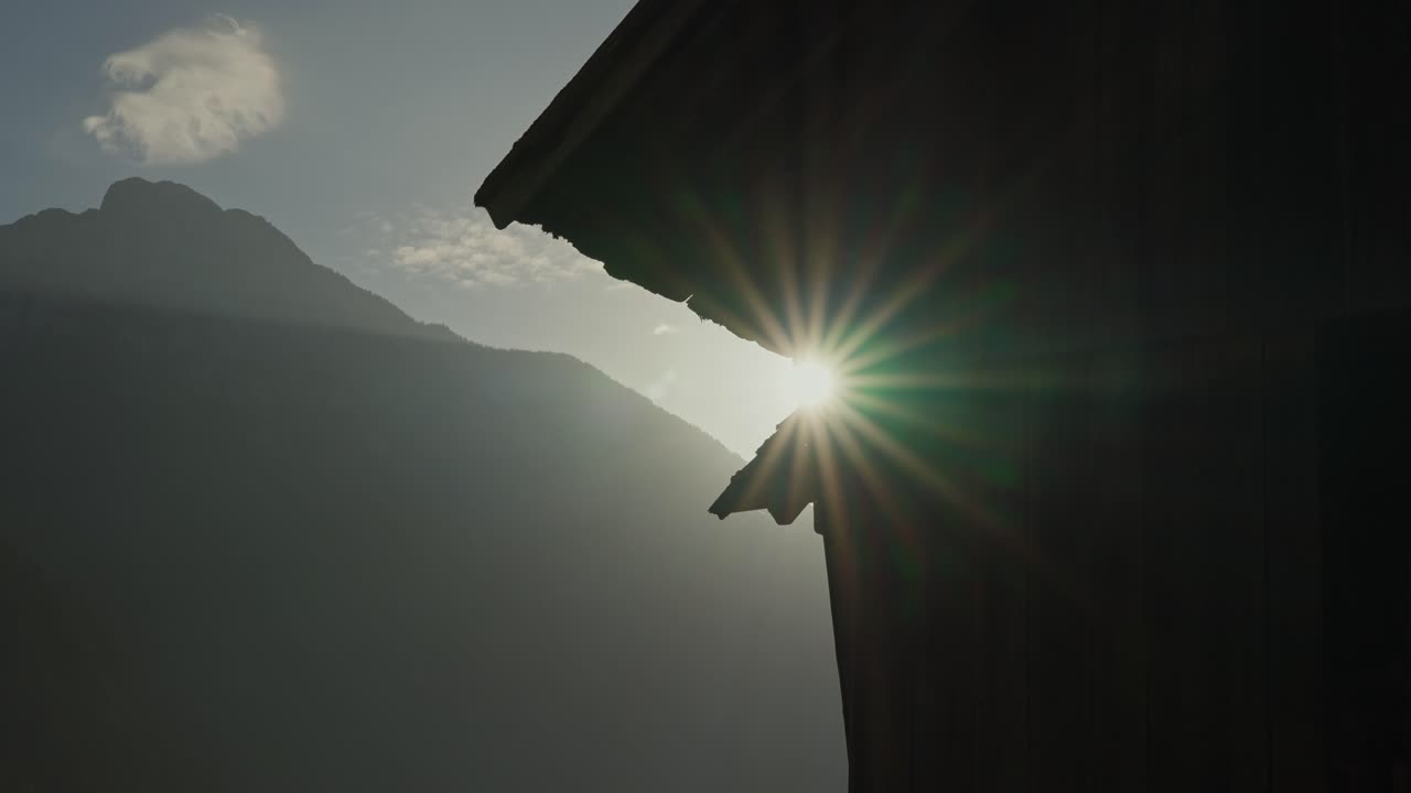 Sunlight shines through a rustic roof in a peaceful mountain setting during early morning.