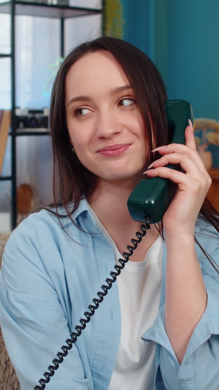 Woman surprised answering vintage retro 90s wired telephone smiling nostalgically happy memories