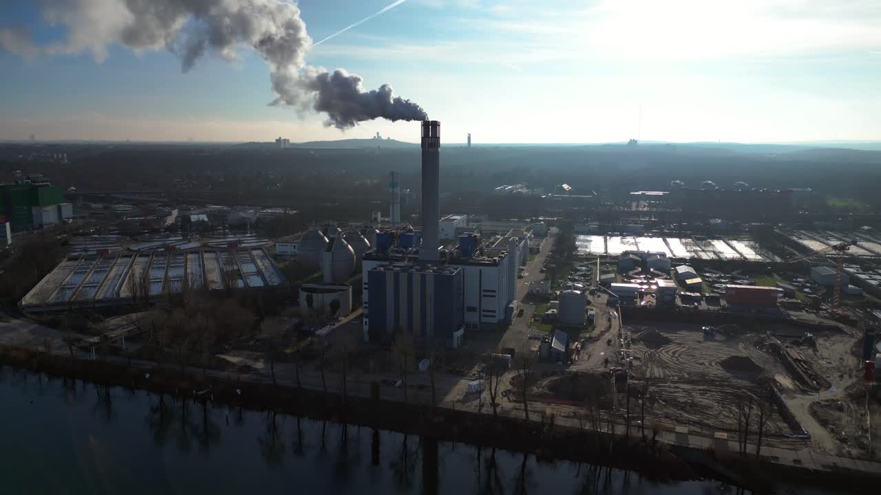 Waste to energy plant emitting smoke from its chimney, located near an urban area, environmental impact of waste. Marvelous aerial view flight descending drone