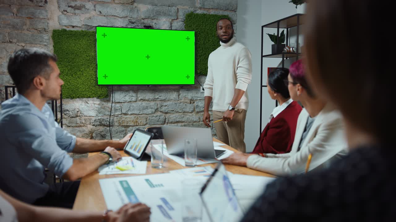 reunión en la sala de conferencias de la oficina: estratega jefe de la compañía negra haciendo una presentación de televisión en pantalla verde a un equipo diverso de empresarios multiétnicos. usando el monitor de televisión de pared de chroma key
