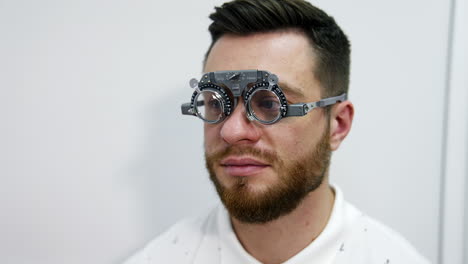 Face of a man in trial frame on eyes. Patient examining his eyesight with a special testing glasses in clinic. Doctor puts lenses into the trial frame. Ophthalmology.