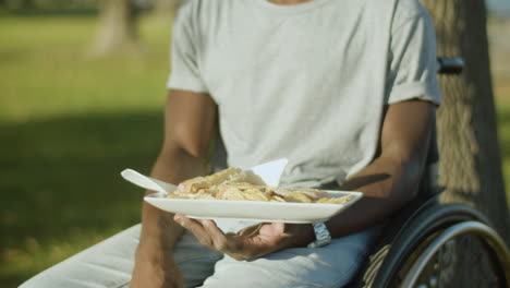 closeup of black man in wheelchair having lunch in city park