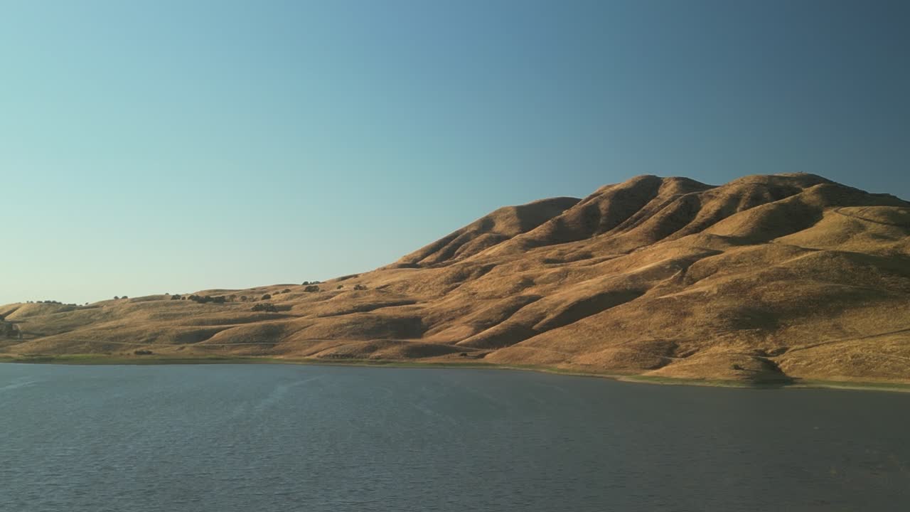 A slow drone shot unveils the Paicines Reservoir, nestled in serene landscapes and bordered by lush fields in Paicines, California.