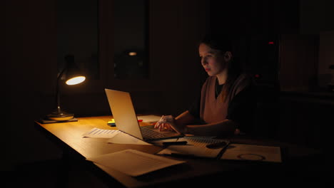 young good looking caucasian woman typing and working on the laptop computer as freelancer while sitting at home in the cozy dark living room with a cat. at night. stay home