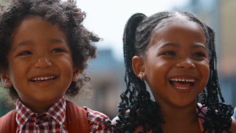 Close-Up-Portrait-Of-Multi-Cultural-Elementary-School-Pupils-Sitting-On-Wall-Outdoors-At-School