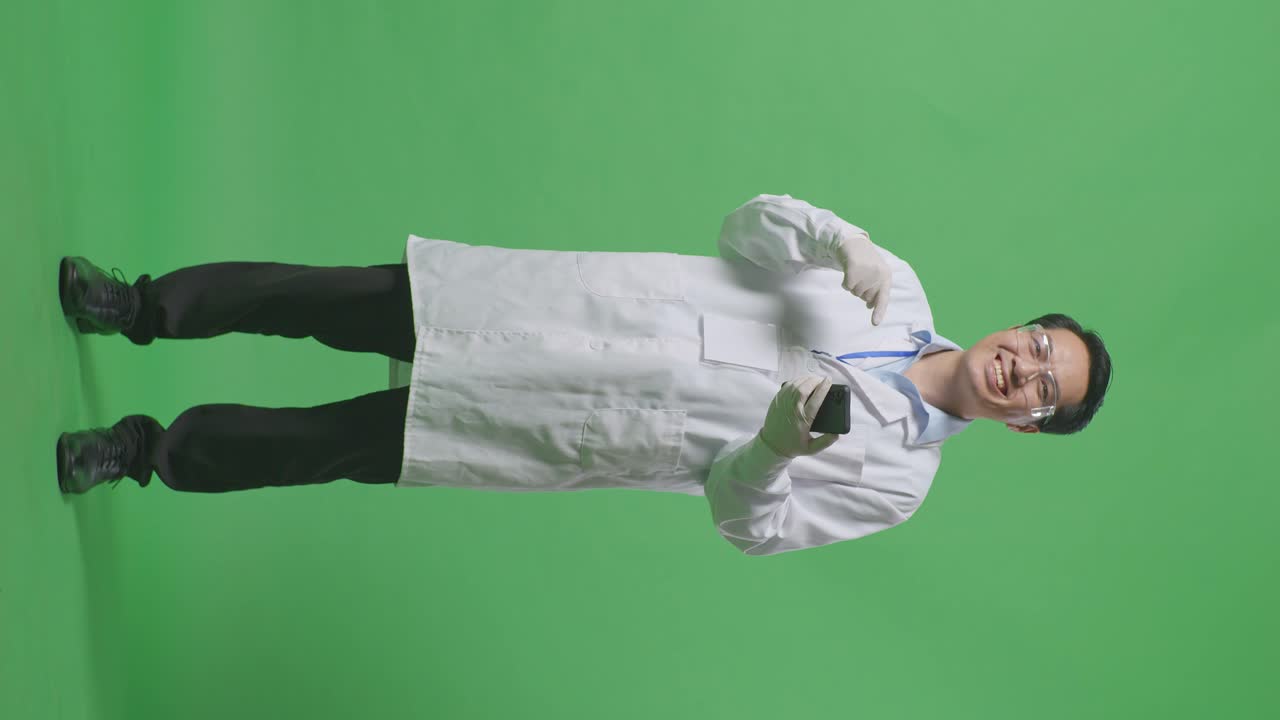 Full Body Of Asian Man Scientist Smiling And Pointing To Smartphone While Standing On The Green Screen Background In The Laboratory