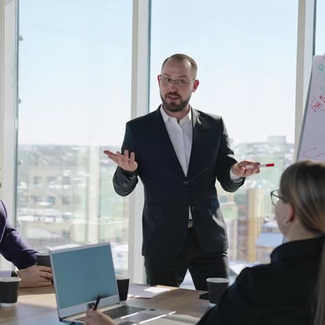 office workers sit at the table with laptops and look at the speaker. the presenter gives a talk emotionally in front of the colleagues. business presentation in the light office