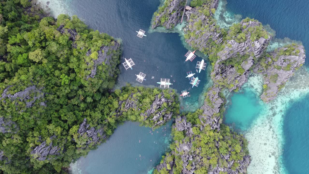Boats and people in clear water amid lush karst cliffs at twin lagoon, coron