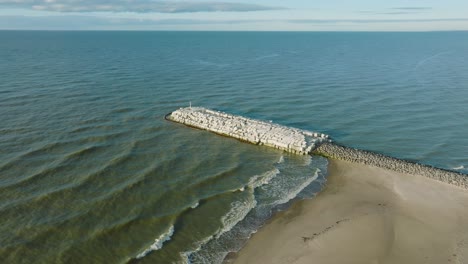 aerial establishing view of protective pier with concrete blocks and rocks at baltic sea coastline at liepaja, latvia, strengthening beach against coastal erosion, drone shot moving forward tilt down