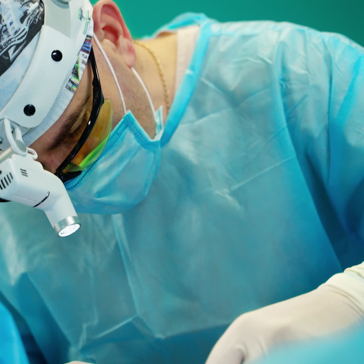 Doctor's face in mask and glasses during operation. Surgeon with magnifying glass on his head performing an operation to a patient. Close-up.