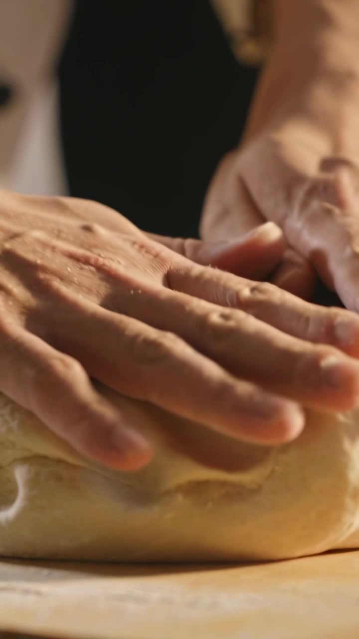 Vertical video: Shaping hands lifting edge, pressing, smoothing dough on floury board for rising