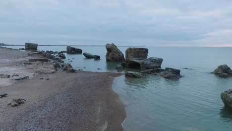 aerial view of abandoned seaside fortification buildings at karosta northern forts on the beach of baltic sea , waves splash, overcast day, ascending drone shot moving forward