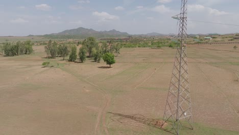 aerial - rising drone shot by power tower revealing vast field with mountain