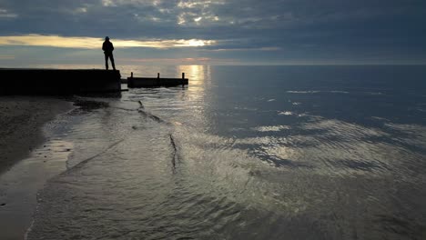 Panorámica-A-Cámara-Lenta-Mar-En-Calma-Con-La-Silueta-Del-Hombre-Al-Atardecer-En-La-Playa-De-Fleetwood-Lancashire-Uk