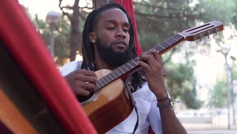 ethnic guy playing guitar in hammock in countryside